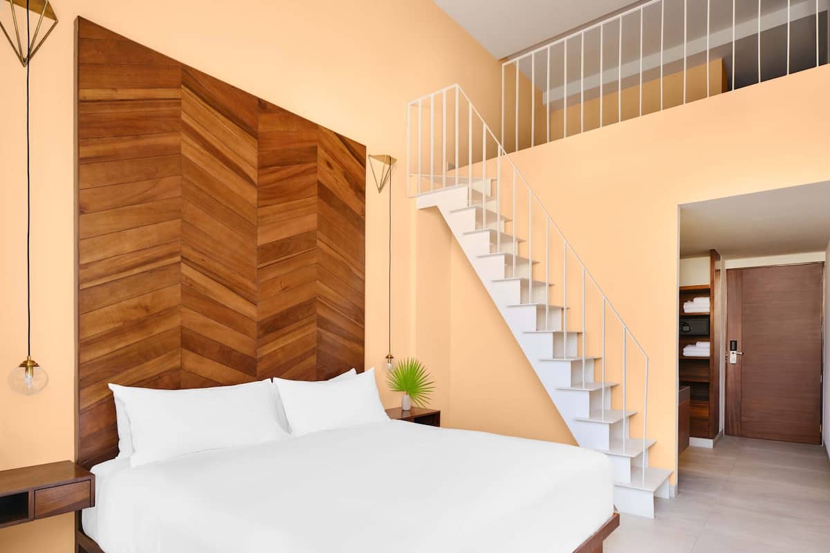 A bedroom with a large bed, a wooden herringbone headboard, a white staircase, and a small plant on a nightstand.