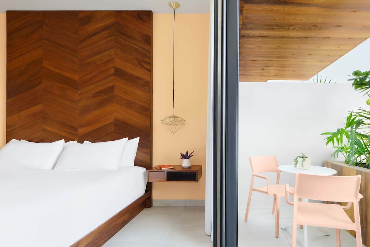 A modern bedroom with a wooden herringbone headboard, a bedside table with a plant, and a small round table with chairs.