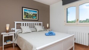 Ein Schlafzimmer mit einem weißen Bett, zwei Nachttischen, einem Fenster mit Blick und einem Bild an der Wand.