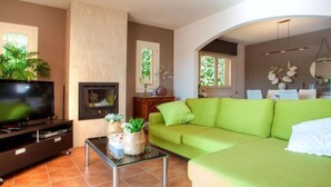 Ein Wohnzimmer mit einem grünen Sofa, einem Flachbildfernseher, einem Kamin und einem Essbereich mit Stühlen.