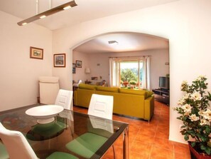Zona de menjador amb taula de vidre i cadires, sofà groc al fons i una planta en test.