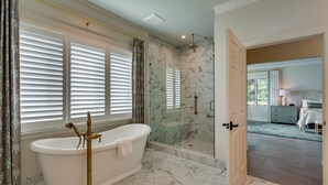 Een badkamer met een vrijstaand bad, een douchecabine met glazen wanden en een vloer van marmer.