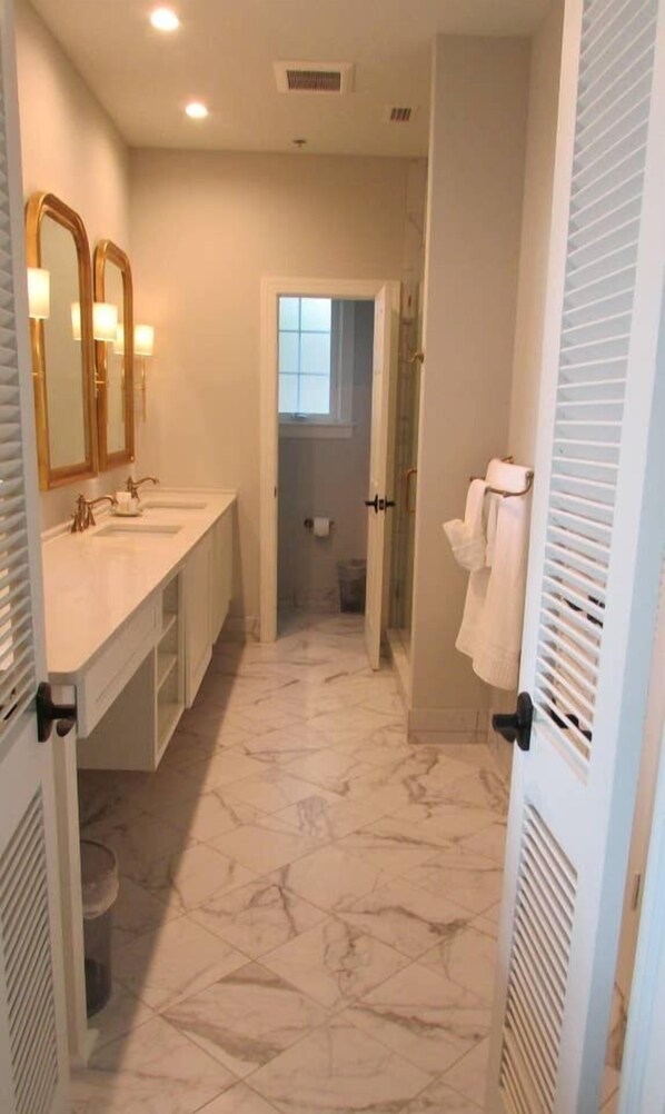 A bathroom with two sinks, a mirror, a shower, and a towel rack. - Azaleana Manor (Orange Park)