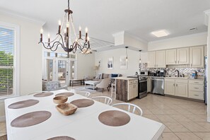A modern kitchen with white cabinets, a dining area with a white table and placemats, and a chandelier.