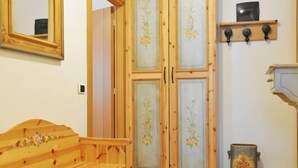 Een houten bank met bloemversieringen, een dubbele deur met bloempanelen, een plank met drie zwarte objecten, en een decoratieve prullenbak.