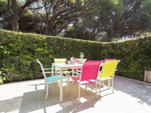 Een terras buiten met een tafel en stoelen, omringd door een haag en bomen.
