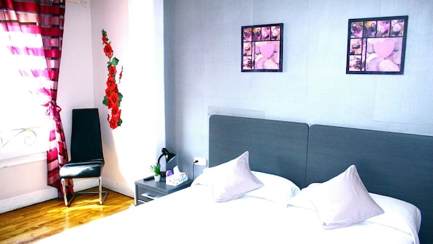 Un dormitorio con cama, almohadas, mesita de noche, una silla y una obra de arte en la pared.
