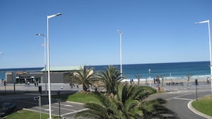Una carretera costera con palmeras, farolas y una playa al fondo.