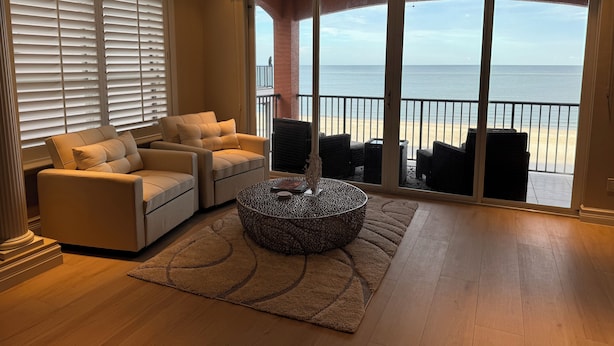 A living room with a beige sofa, a round coffee table, and a view of the beach through large sliding glass doors. - 30 STEPS - BEACHFRONT LUXURY OASIS! PRIVATE POOL AND HOT TUB!  (Fort Myers Beach)