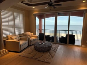 A living room with a beige sofa, a round coffee table, and a view of the beach through large sliding glass doors. - 30 STEPS - BEACHFRONT LUXURY OASIS! PRIVATE POOL AND HOT TUB!  (Fort Myers Beach)