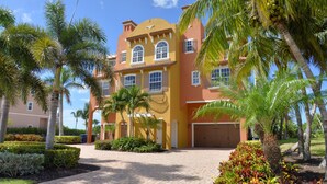 A multi-story building with a yellow facade, palm trees, and a paved driveway. - 30 STEPS - BEACHFRONT LUXURY OASIS! PRIVATE POOL AND HOT TUB!  (Fort Myers Beach)