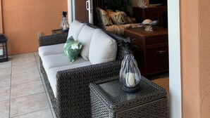 A balcony with wicker furniture, a white sofa, and a glass table. - 30 STEPS - BEACHFRONT LUXURY OASIS! PRIVATE POOL AND HOT TUB!  (Fort Myers Beach)