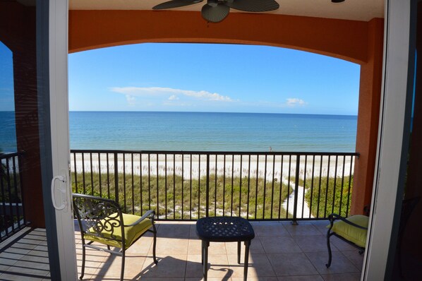 A balcony with a view of the ocean, a chair, and a table.