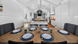 Un vaste espace dédié à la salle à manger, avec une longue table dressée pour six personnes, entourée de chaises grises à l’assise rembourrée.