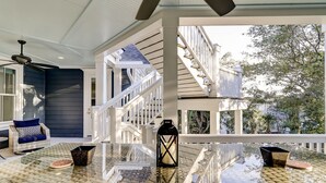 Un espace extérieur abrité, doté d'une table en verre, d'un fauteuil en osier, d'une lanterne et d'un escalier menant à une terrasse.