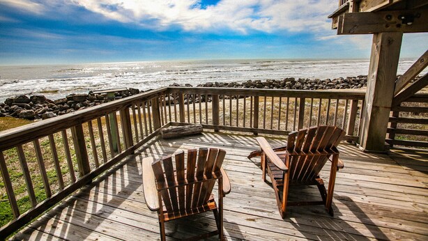 A wooden deck with two Adirondack chairs overlooking a rocky beach and the ocean.