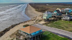 A coastal property with a beach view, a wooden structure with a balcony, and a road leading to the beach.