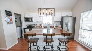 A modern kitchen with a central island, bar stools, stainless steel appliances, and a hanging light fixture.