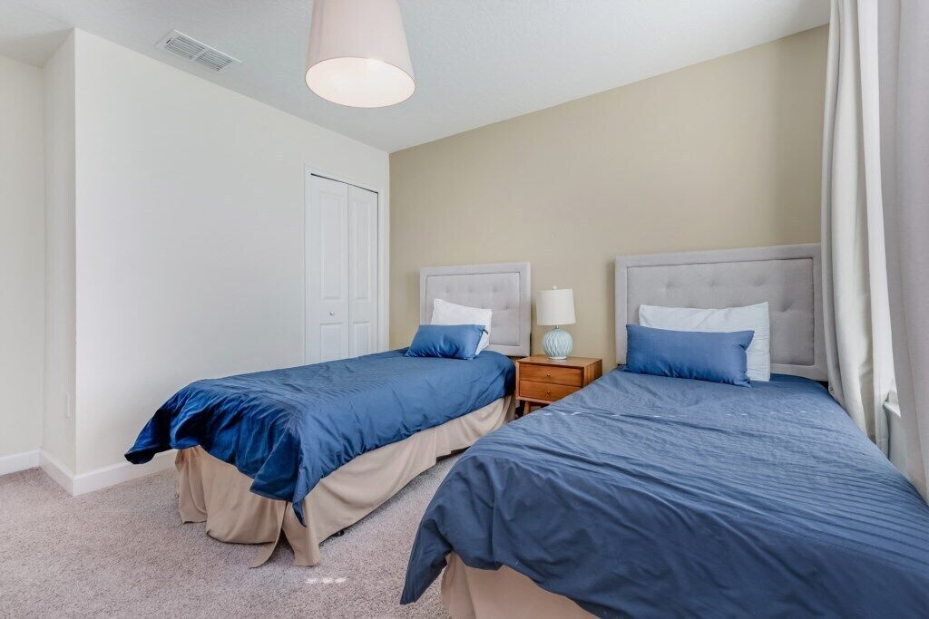 A bedroom with two beds, beige walls, and a white door.