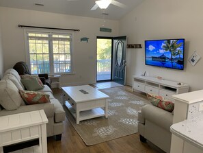 Relax in this open-plan living space with a large flat-screen TV, comfortable seating area, and sliding glass door leading to an outdoor area.