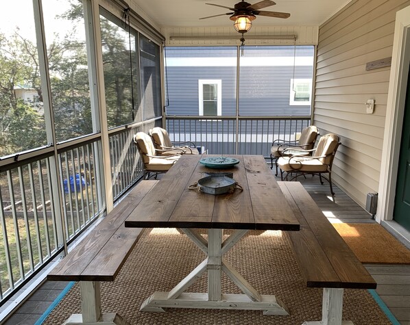 A wooden deck with a table and chairs, a ceiling fan, and a view of a house in the background.