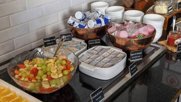 Um buffet com diversas opções de comida, incluindo salada de frutas, iogurte e outros pratos prontos.
