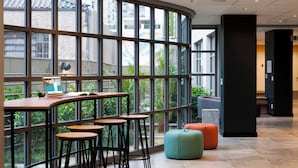 Un espacio interior moderno con ventanas amplias, una pared curva y una zona de estar con taburetes y un banco acolchado.