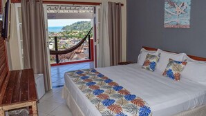 Quarto de hotel com uma cama, um banco de madeira, vista de uma cidade pela janela e uma rede do lado de fora.