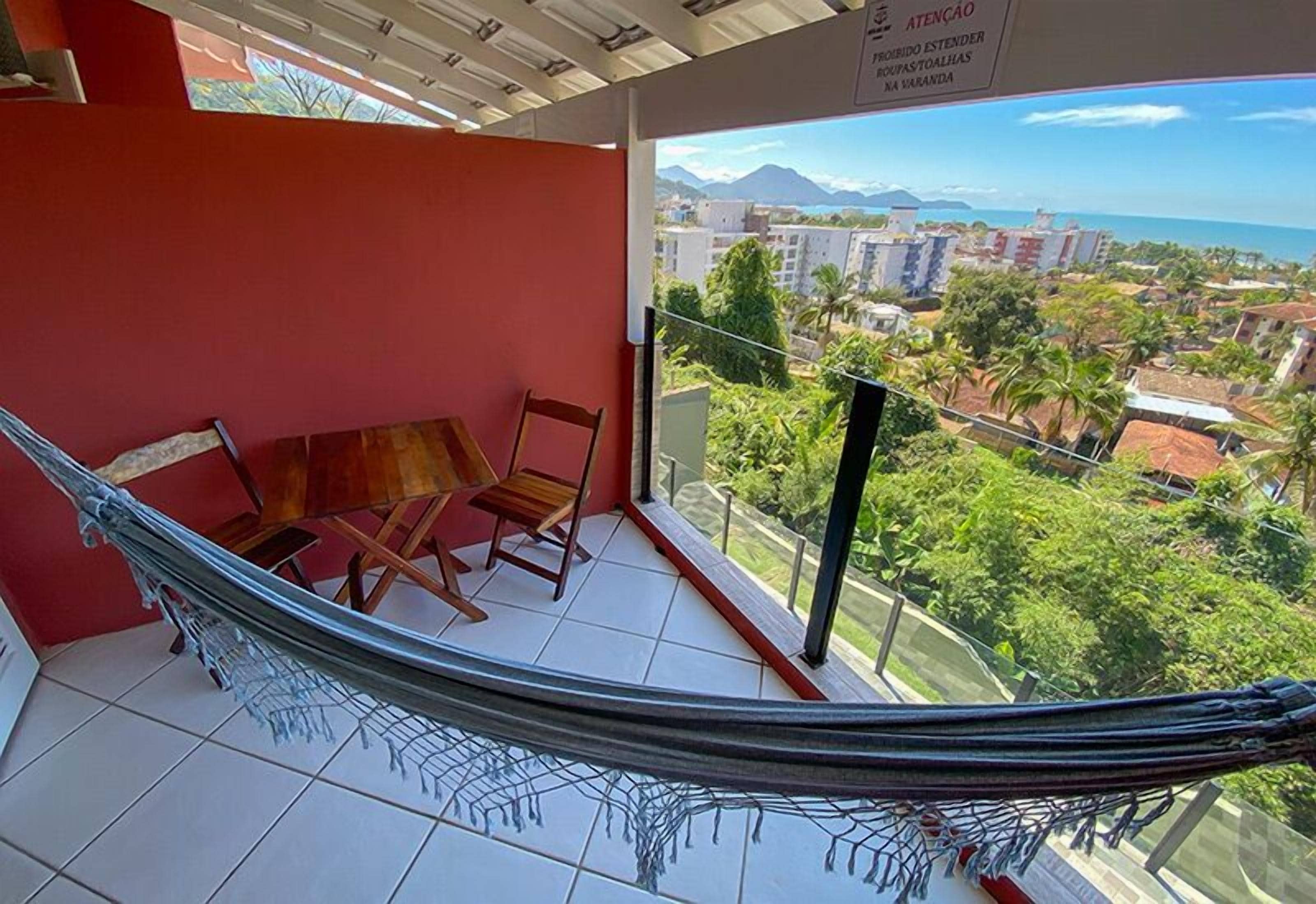 Uma varanda com uma rede, cadeiras e vista para uma paisagem urbana com montanhas.
