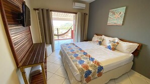 Quarto com cama, um banquinho de madeira, uma TV e vista para o exterior.