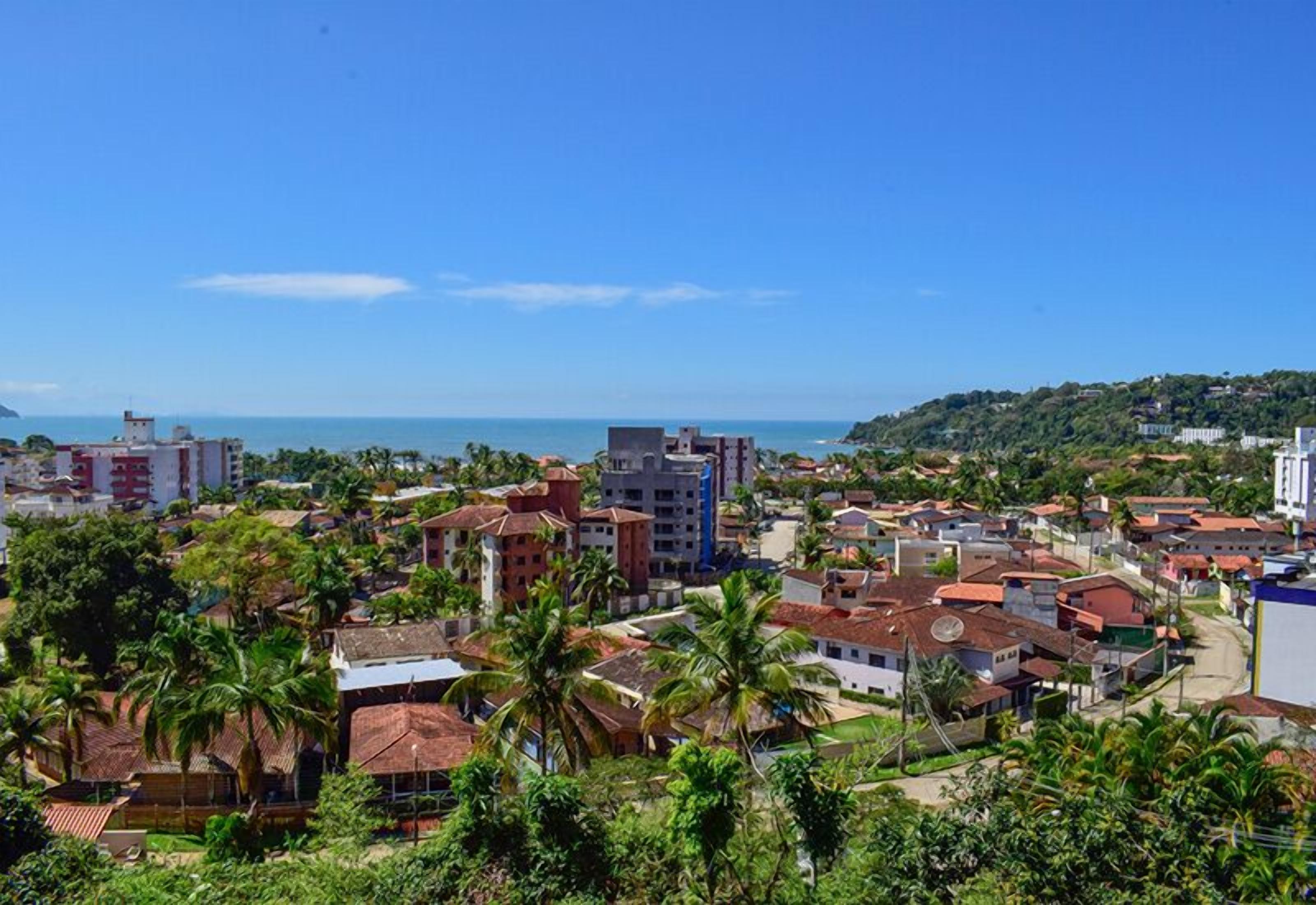 Uma vila costeira com edifícios, palmeiras e vista para o mar.