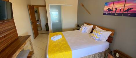 A hotel room with a bed, wooden bench, and a painting on the wall.
