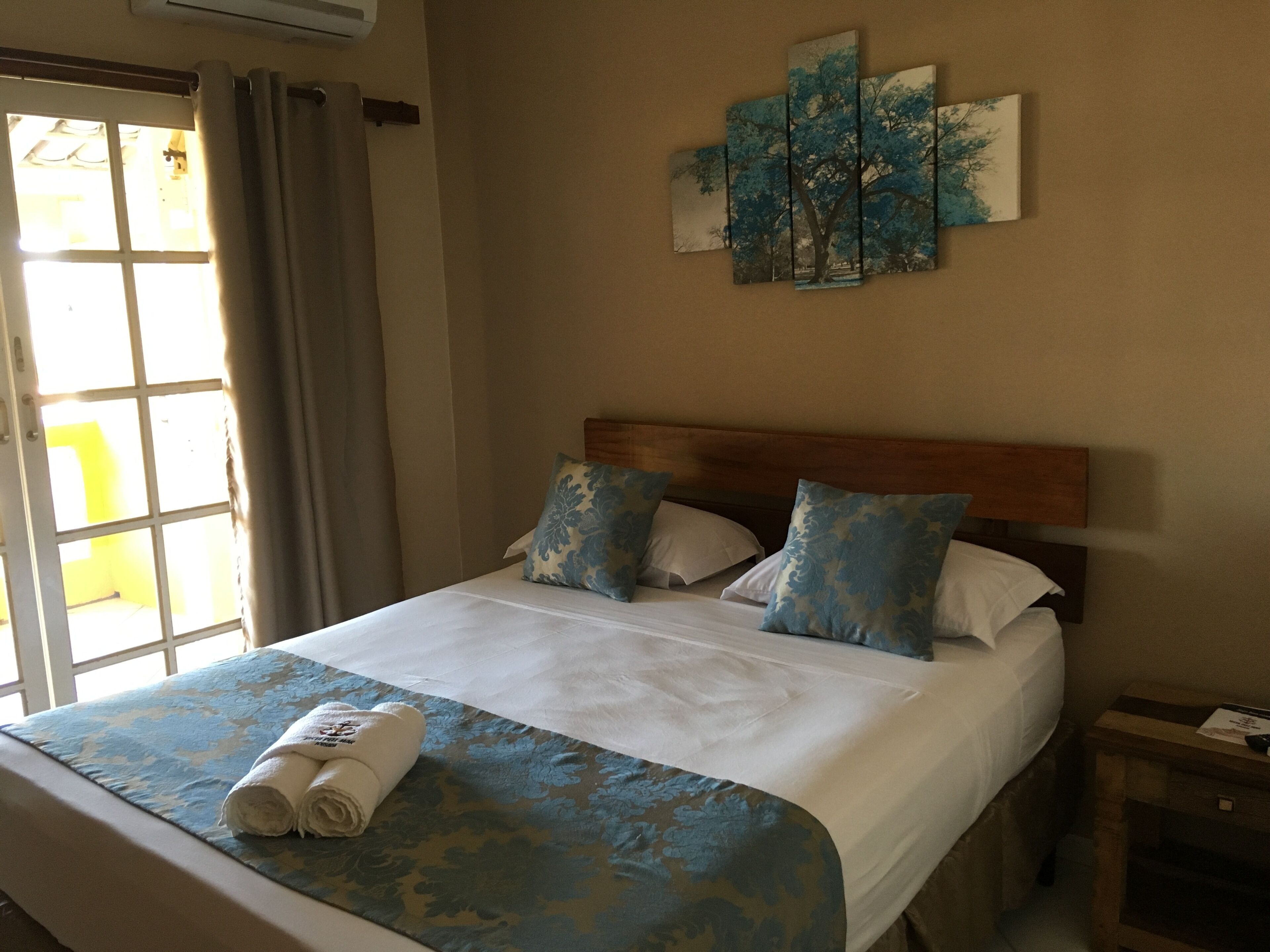 A hotel room with a bed, a headboard, a nightstand, a wall art piece, and a window with curtains.
