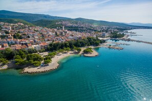 An aerial view of a coastal town with a marina, clear turquoise waters, and a mountainous backdrop. - Apartments Feda (Crikvenica)