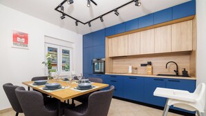 A modern kitchen with blue cabinets, a wooden countertop, and a dining area with a table and chairs. - Apartment Mladen (Crikvenica)