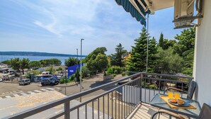 A balcony with a table set for breakfast, overlooking a parking area and a body of water. - Apartment Mladen (Crikvenica)