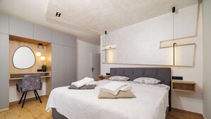 A modern bedroom with a large bed, bedside tables, a desk with a chair, and a wall-mounted mirror. - Apartment Mladen (Crikvenica)