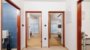A hotel corridor with wooden doors, a visible bathroom on the left, a bed and bedside table in the middle, and a wardrobe on the right. - Apartment Mladen (Crikvenica)