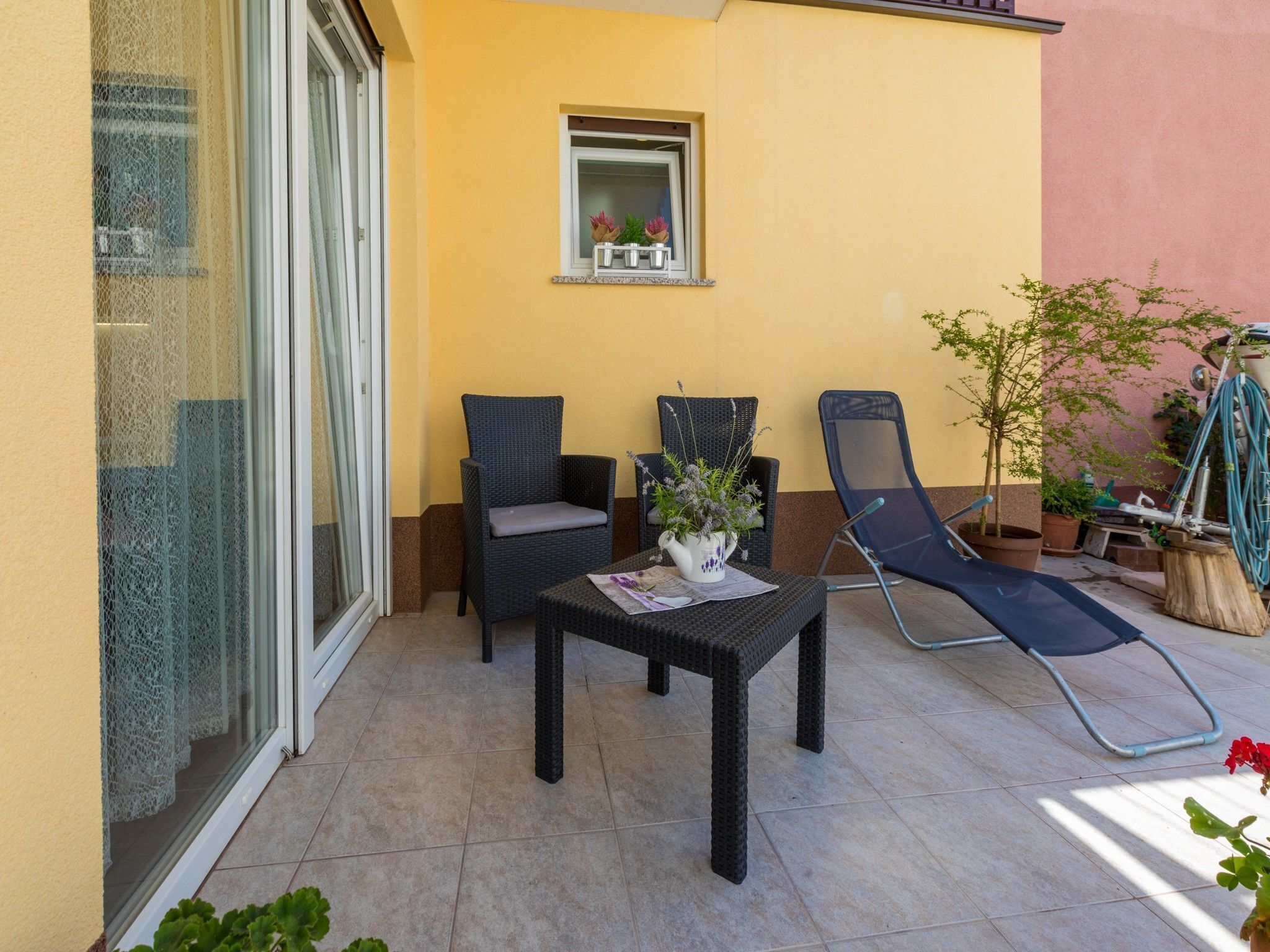 Eine Terrasse mit zwei Korbstühlen, einem kleinen Tisch mit einer Vase und einem Blumentopf.