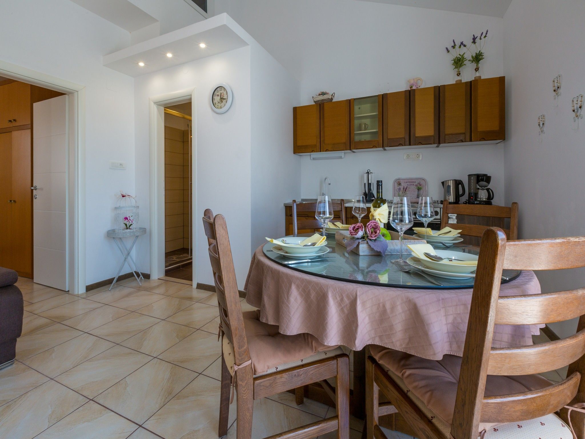 A dining area with a round glass table, wooden chairs, and a clock on the wall.
