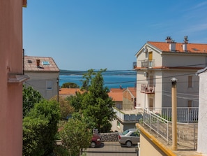 A coastal residential area with terracotta-roofed buildings, a clear blue sky, and a view of the sea.