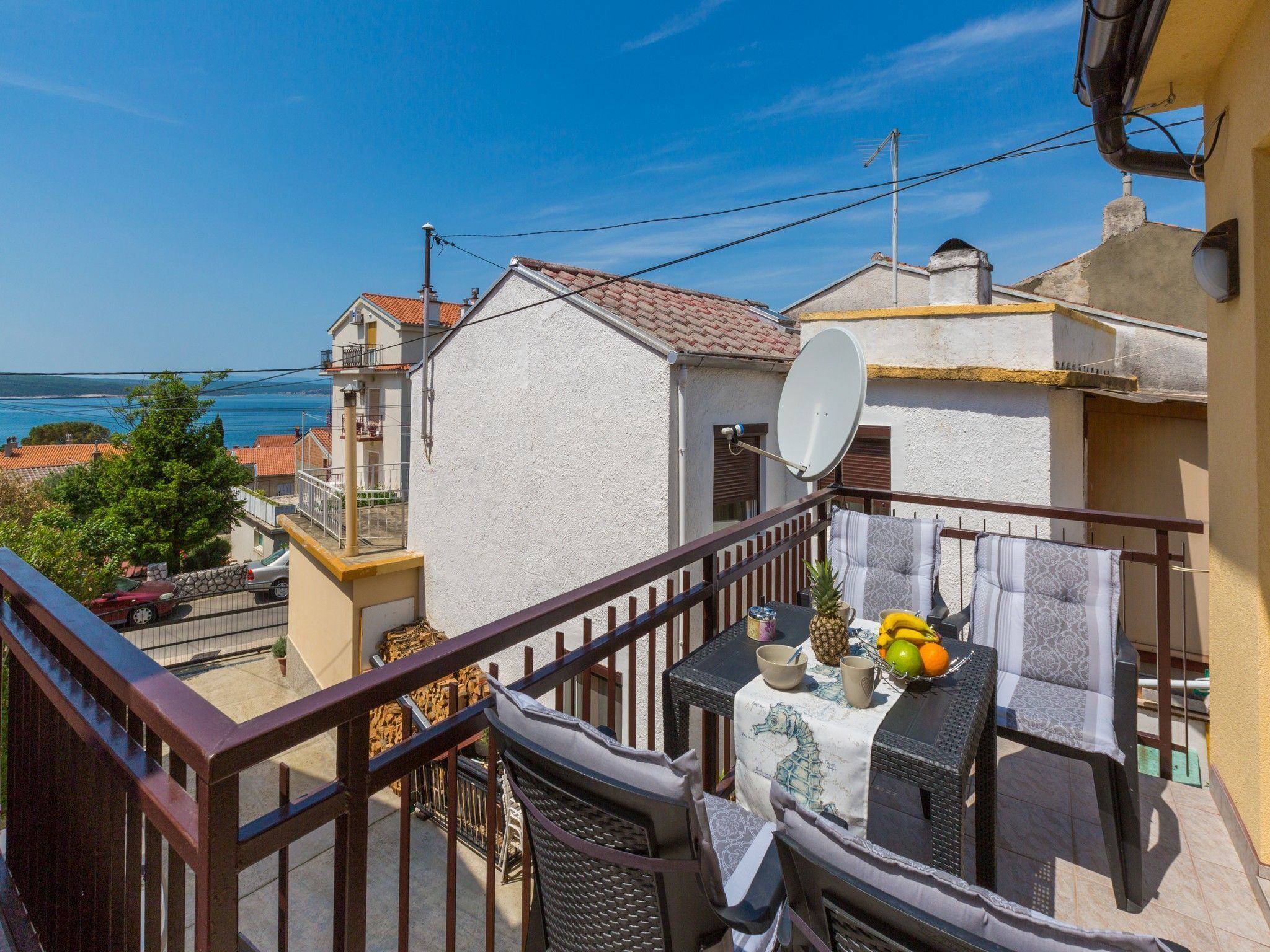 Een balkon met een eettafel, met uitzicht op een kustgebied met huizen en de zee.
