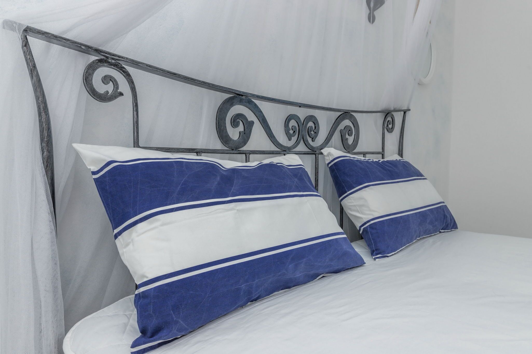 A bed with a metal headboard and two pillows with blue and white stripes.
