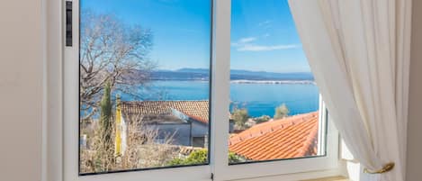 Ein Fenster mit Blick auf eine Küstenlandschaft, einschließlich eines Gewässers und Gebäude mit roten Ziegeldächern.
