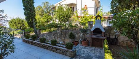 A courtyard with a stone pathway, potted plants, a stone wall, and a building with a balcony.