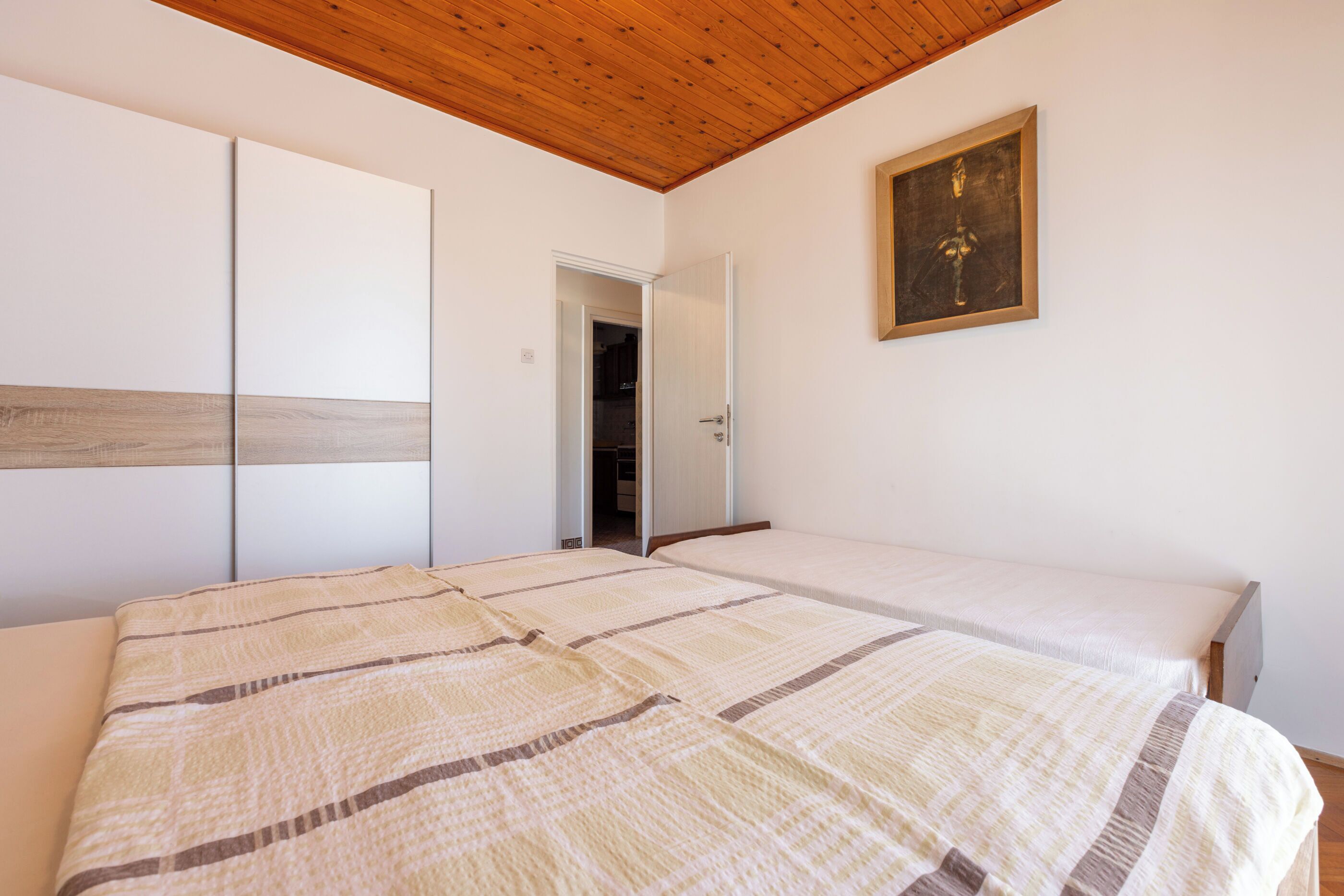 A bedroom with a large bed, a wardrobe, and a door leading to another room.