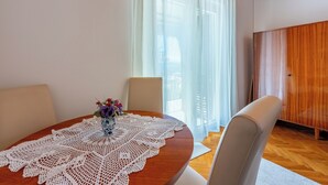 Une table ronde en bois, recouverte d’une nappe en dentelle blanche, deux chaises et un vase rempli de fleurs.