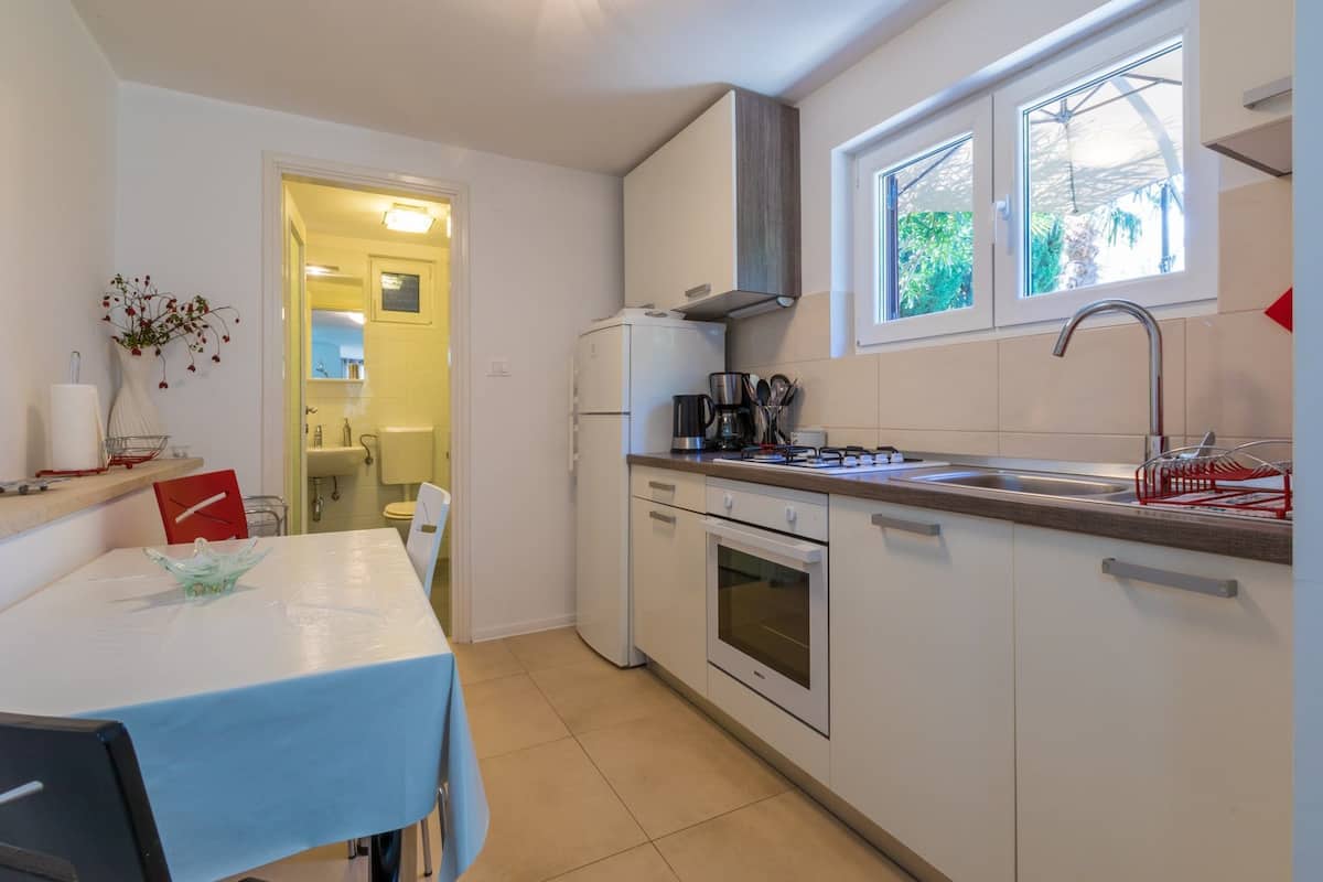 A compact kitchen with white cabinets, a built-in oven, a coffee maker, and a window with a view of greenery.
