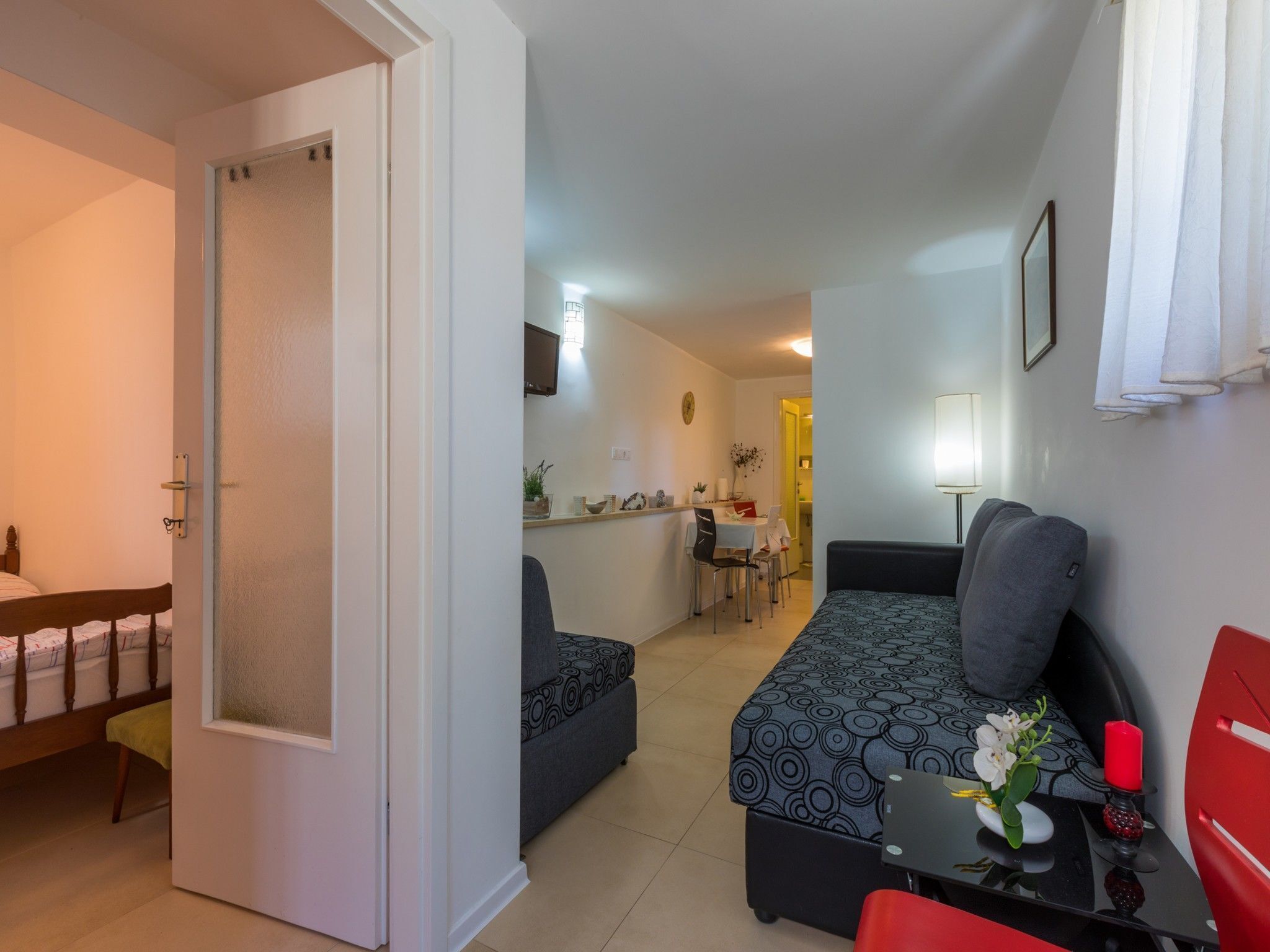 Un espacio habitable pequeño con cama, sofá, una mesita con un florero y una silla roja.