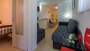 Un espace de vie compact comprenant un lit, un canapé, une petite table avec un vase de fleurs et un fauteuil rouge.